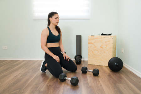Catching my breath. Attractive young woman working out at home and taking a break from her functional training with dumbbell weightsの写真素材