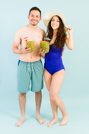 Full length of an hispanic boyfriend and girlfriend drinking a pina colada cocktail next to the pool. Attractive couple going on a summer vacationの写真素材