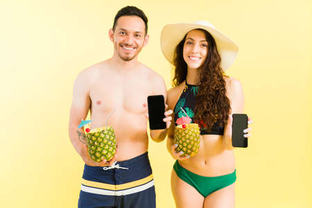 Portrait of an attractive latin man and caucasian woman showing their smartphone screen and smiling...