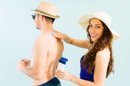 Portrait of a beautiful woman in a swimsuit smiling and making eye contact while applying sunscreen...