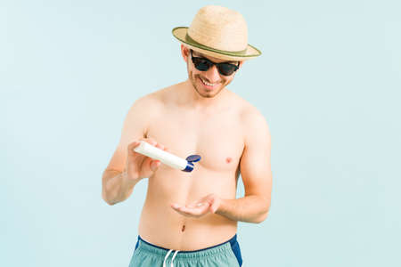 Healthy man applying sunblock lotion in his body and face to avoid getting sunburned by the pool or in the beachの写真素材