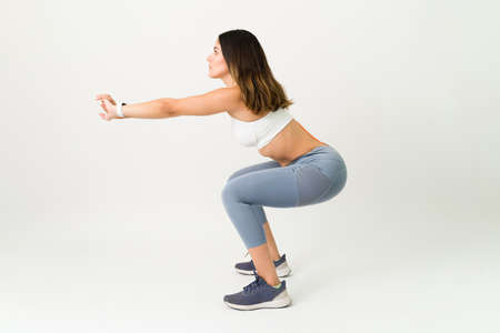 Focused on finishing my workout routine. Sporty woman in activewear doing squat exercises to...
