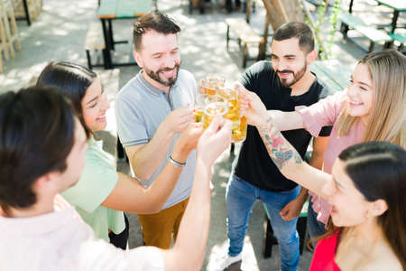 Thrilled group of friends in their 20s making a toast with beers and laughing. Attractive friends...