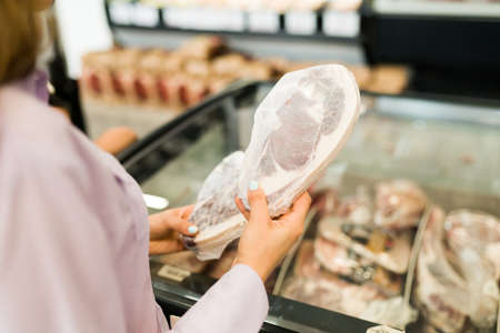 Rear view of an hispanic young woman hands holding a frozen steak at the butcher shop and choosing what meat to buyの写真素材