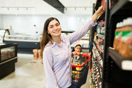 These are the best products at the store. Beautiful young woman smiling and looking at the camera while choosing food brands at the grocery marketの写真素材