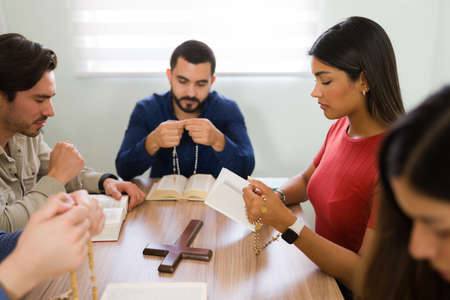 Diverse group of young people in a religious community praying with a catholic rosary during their...