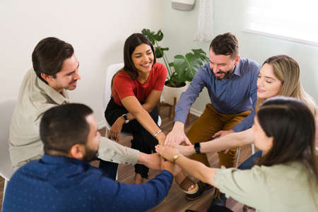 Members of a support group putting their hands together to make a high five. Cheerful young women...