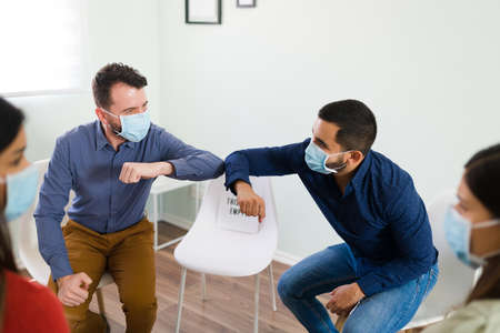 Elbow bump. Two young men with face masks saying hello before starting their alcoholic anonymous...