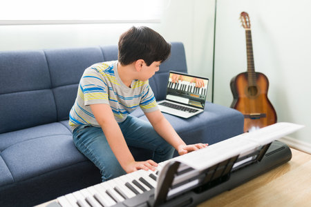 Young boy following the instructions of the music teacher and learning to play the piano. Caucasian kid taking art lessons on an online video callの写真素材