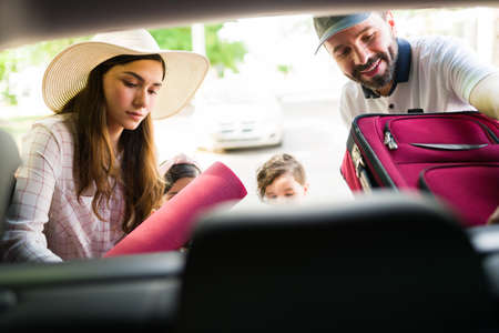 Happy mom and dad putting the luggage in the trunk of the car. Beautiful family getting ready to go to a vacation spot on the holidaysの写真素材