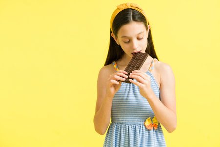 Adorable preteen girl eating delicious chocolate. Beautiful young girl with sugar cravings taking a bite of a sweet candy barの写真素材