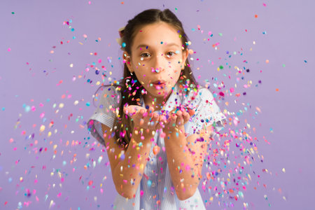 Adorable young girl blowing and playing with confetti during a happy celebration. Beautiful girl celebrating her birthdayの写真素材
