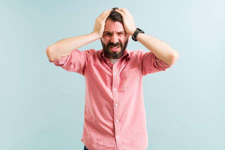 Portrait of a sick handsome man making eye contact while rubbing his head because of a bad migraine...