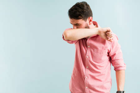 Sick man coughing in the inside of his arm or elbow. Latin man preventing the spread of the flu or virusの写真素材