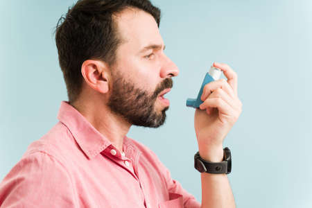 Profile of a handsome man about to use a reliever inhaler because he is having an asthma attack...