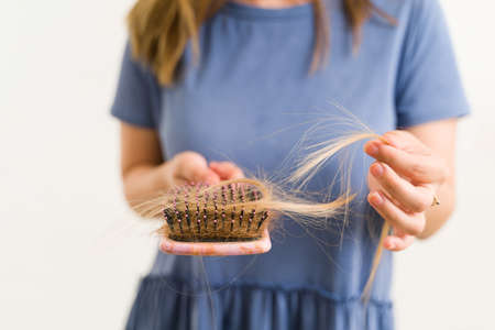 Close up of a young woman holding a brush with a lot of tangled hair after brushing. Woman suffering...