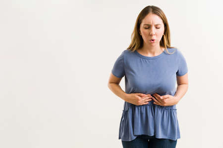 Indigestion concept. Attractive young woman in her 20s rubbing her abdomen because of a bad stomach acheの写真素材
