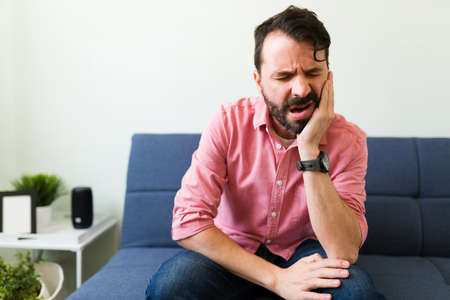 Sick man in his 30s suffering from a toothache at home. Latin man in pain needs to go to the dentistの写真素材