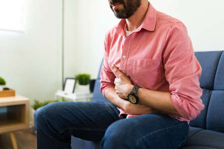 Sick latin man with a lot of nausea touching his abdomen because of a bad stomachache and a...