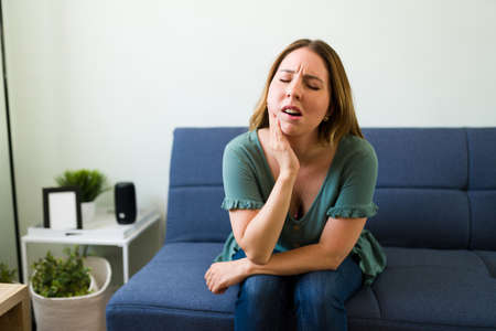 Pained woman in her 20s suffering from a toothache at home. Caucasian woman in pain needs to go to the dentistの写真素材