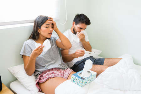Getting down with the flu. Sick beautiful woman and man with a fever and cough suffering from a bad...