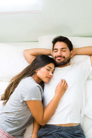 High angle of a handsome hispanic man smiling while sleeping with his girlfriend and having a happy...