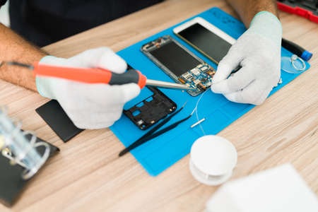 Close up of a technician with gloves soldering and fixing the motherboard of an old smartphone at his repair shop deskの写真素材