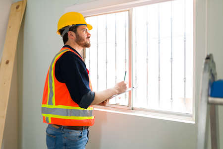 Focused inspection expert with a safety helmet checking the quality of the windows and walls in the construction siteの写真素材