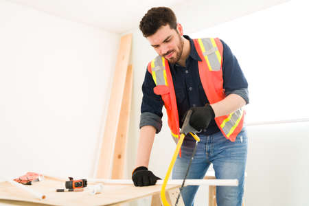 Happy male contractor cutting new pipelines with a saw. Hispanic plumber working at the construction siteの写真素材