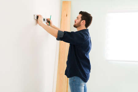 Attractive man in his 30s using a level to check a new wall. Handyman working on his home to do some...
