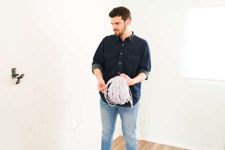 Installing a new light switch. Attractive man holding a lot of cables and changing the electric...