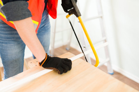 Hardworking plumber wearing safety gloves while cutting with a saw some pipes to build a new...