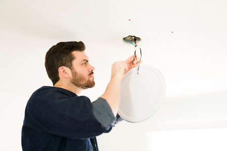 Professional hispanic electrician fixing the electrical system in the ceiling and cutting some cables at homeの写真素材