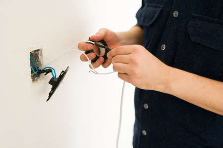 Close up of the hands of a young man hands repairing the broken switch and doing home renovationsの写真素材