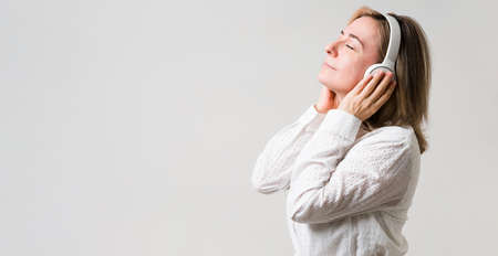 Profile of a relaxed middle aged woman with her eyes closed and headphones listening to relaxing music next to copy spaceの写真素材