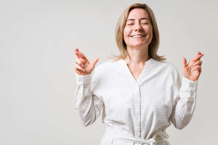 I am feeling lucky. Happy caucasian old woman with her fingers crossed and smiling while asking for...