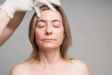 Attractive elder woman in her 50s getting a cosmetic procedure with botulinum toxin to erase her...