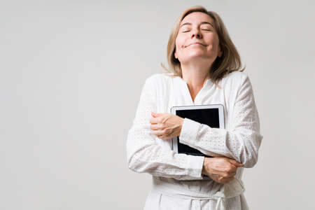 I love technology. Super happy caucasian woman in her 50s hugging her tablet and enjoying some entertainment onlineの写真素材