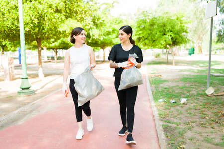 Gorgeous women best friends talking and catching up while picking up trash in the park after exercising together outdoorsの写真素材