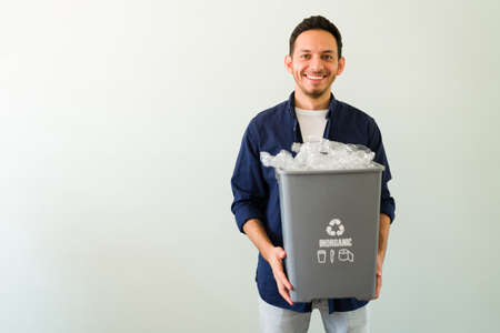 Portrait of a handsome hispanic man smiling and making eye contact while carrying a bin with recycling materialの写真素材