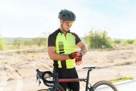 Hispanic young cyclist counting the calories on a smartwatch after finishing his workout on his road...