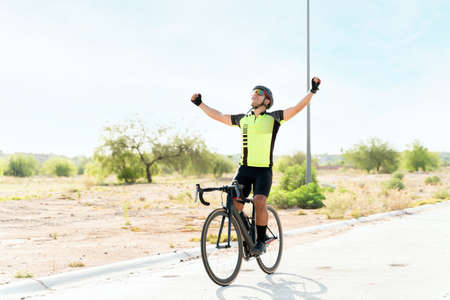 Handsome young man celebrating a victory. Male cyclist winning the race and spreading his arms while riding his road bikeの写真素材