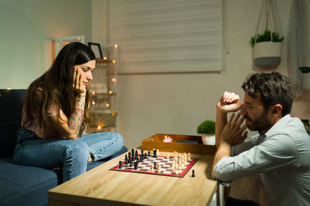Enjoying a board game. Focused young wife and handsome husband playing a match of chess during a date night at homeの写真素材
