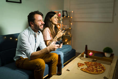 Always having fun with you. Cheerful couple playing video games and eating pizza during a chill casual date at homeの写真素材