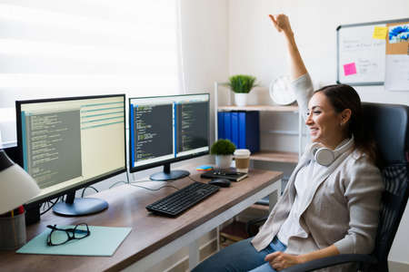 Yes, my program works! Successful excited woman celebrating and raising her arm in victory after finishing writing code for a software appの写真素材