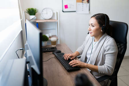 Focused young woman working from home as a sales representative. Hispanic woman with a headset...