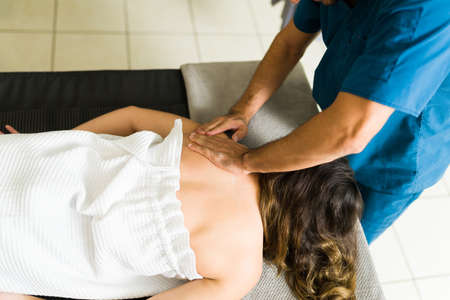 Caucasian patient lying on the massage table and receiving a shoulder massage. Professional physical therapist giving a back rubの写真素材