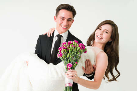 Just married. Romantic husband carrying in his arms her cheerful wife during their wedding reception