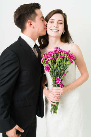 We are getting married! Handsome man in love kissing on the cheek his gorgeous smiling wife on their wedding ceremonyの写真素材
