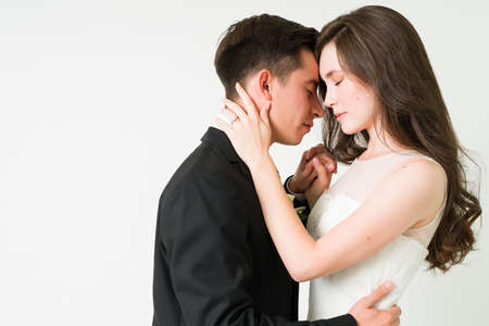 Profile of an adorable young bride and groom in love hugging face to face while closing their eyes for a romantic momentの写真素材